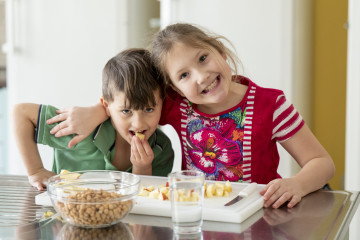 Ein Bub und ein Mädchen lachen und essen Apfelstücke, Schüssel mit Kichererbsen steht vor ihnen