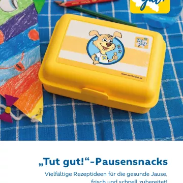 gelbe Jausenbox auf blau kariertem Geschirrtuch, links davon ein bunter Papierdrache