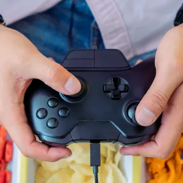 Person hält einen Gamecontroller über Schalen mit Snacks