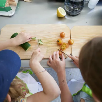 © Johannes Hloch Kinder schneiden Gurke und Tomaten auf einem Holzbrett
